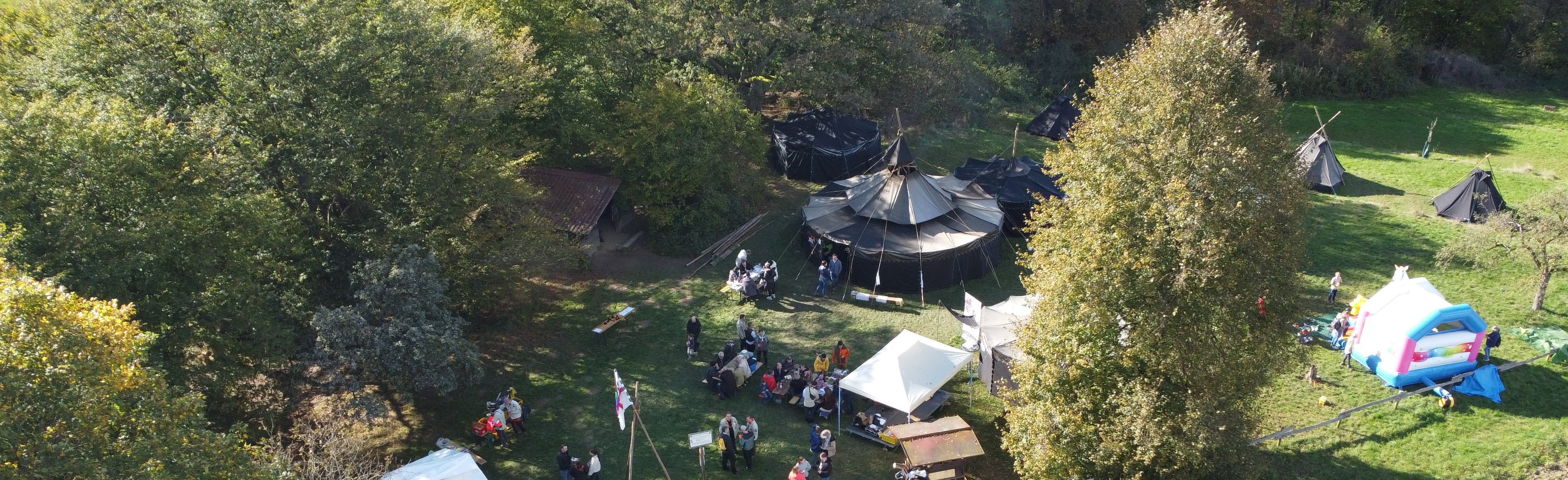 Zeltplatz mit Kothen, Jurten und Menschen aus Vogelsicht im Sonnenschein